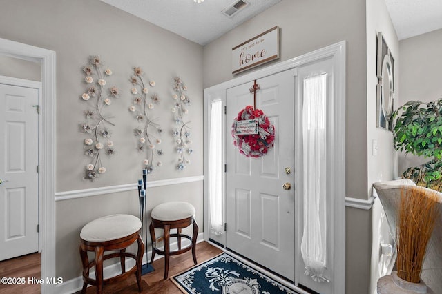 entrance foyer featuring baseboards, a textured ceiling, visible vents, and wood finished floors