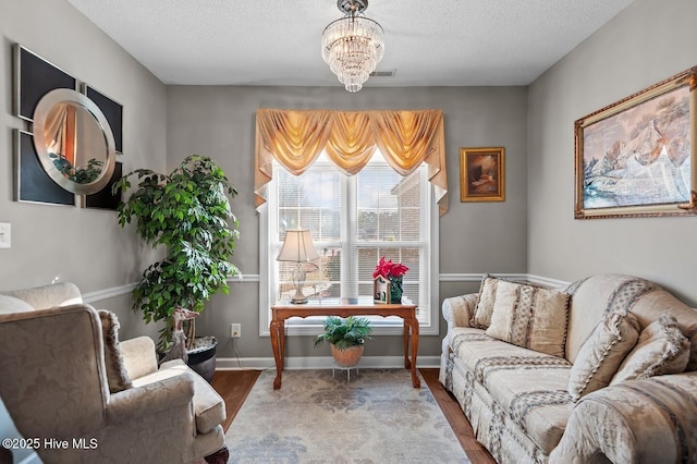 living area with a notable chandelier, a textured ceiling, baseboards, and wood finished floors