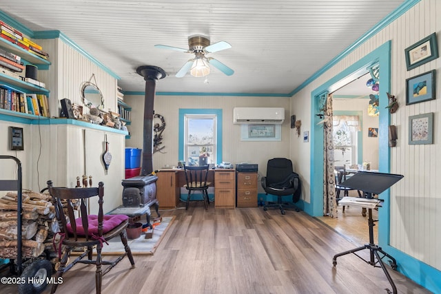 office space with a ceiling fan, a wall unit AC, ornamental molding, wood finished floors, and a wood stove