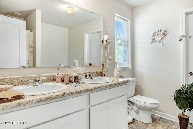 full bath with baseboards, a sink, toilet, and double vanity