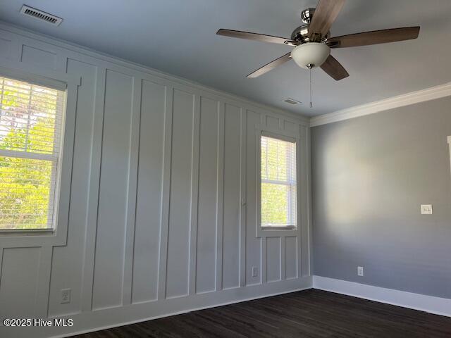 empty room with crown molding, a decorative wall, visible vents, and dark wood-type flooring