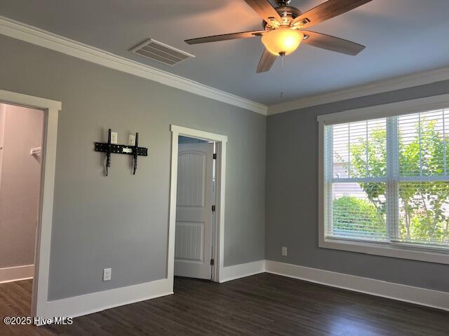 spare room with dark wood finished floors, crown molding, visible vents, and a wealth of natural light