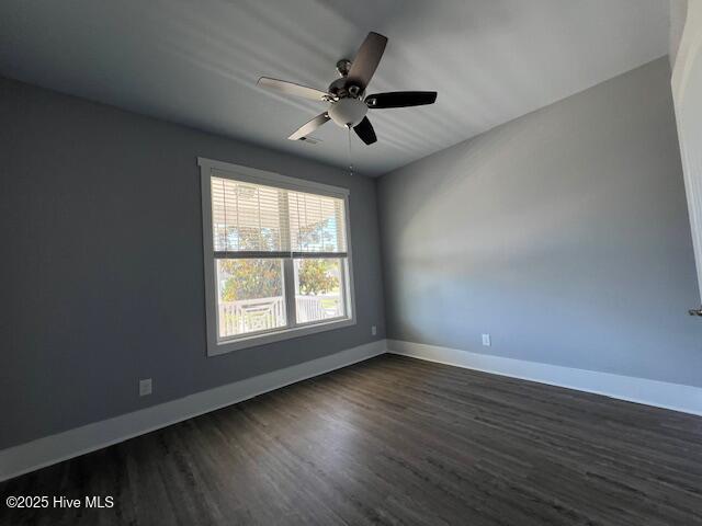 empty room with dark wood finished floors, a ceiling fan, and baseboards