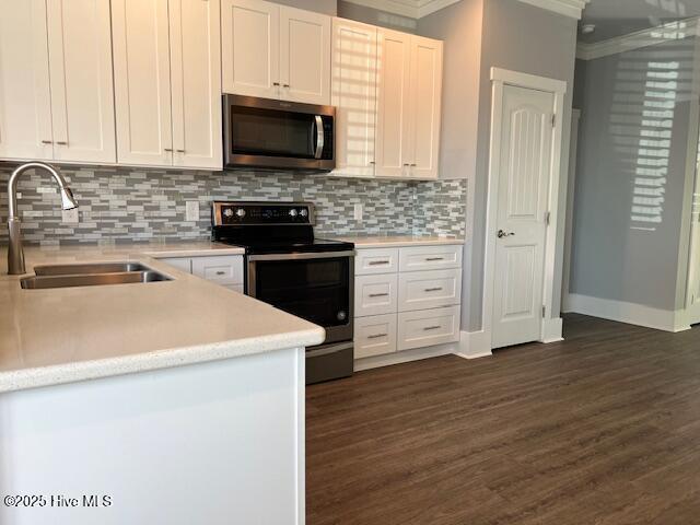 kitchen with dark wood-type flooring, a sink, white cabinetry, stainless steel appliances, and light countertops