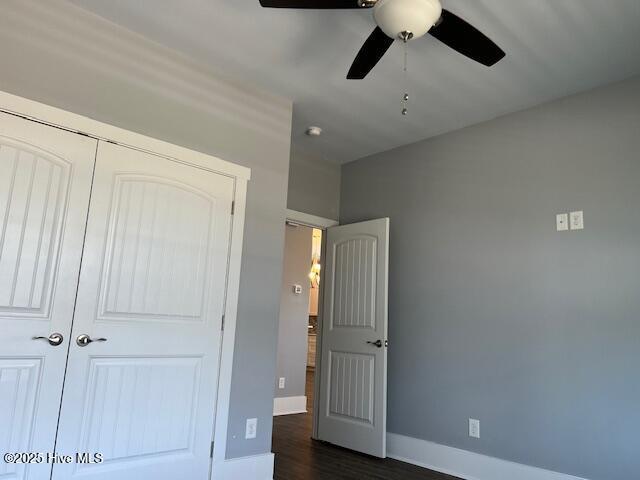 unfurnished bedroom featuring a closet, dark wood finished floors, a ceiling fan, and baseboards