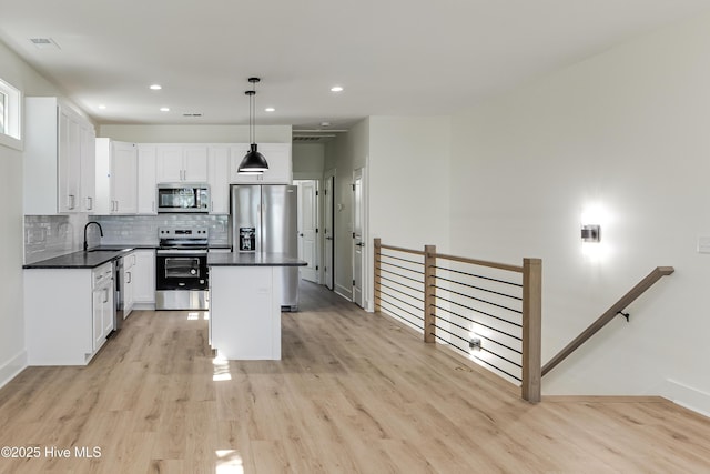 kitchen featuring a sink, a kitchen island, appliances with stainless steel finishes, backsplash, and dark countertops