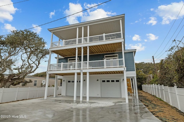 coastal inspired home with a garage, fence, driveway, and a balcony