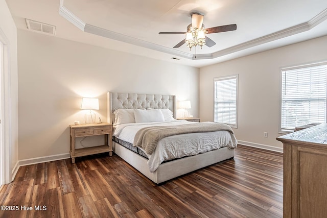 bedroom with baseboards, visible vents, a raised ceiling, ornamental molding, and dark wood-style flooring