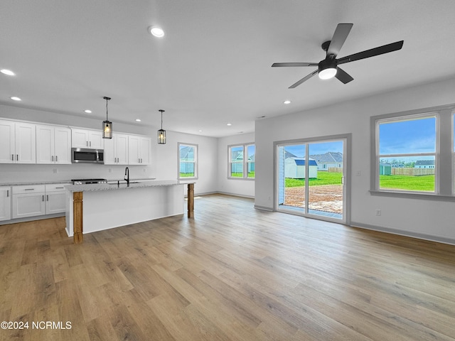 kitchen with recessed lighting, a sink, open floor plan, light wood finished floors, and stainless steel microwave