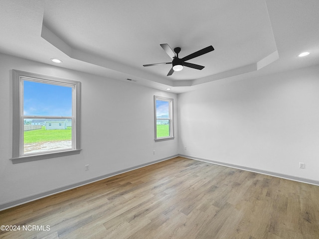 empty room featuring baseboards, a tray ceiling, recessed lighting, and light wood-style floors