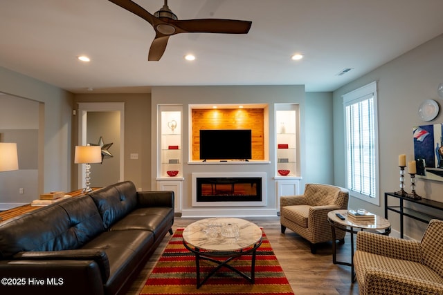 living room with visible vents, a glass covered fireplace, ceiling fan, wood finished floors, and recessed lighting