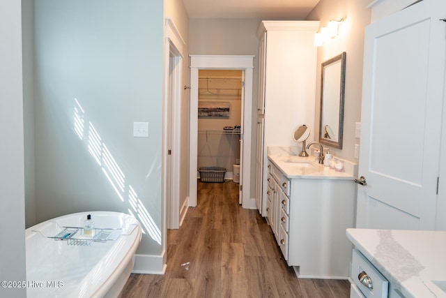 bathroom featuring wood finished floors, vanity, baseboards, a soaking tub, and a walk in closet