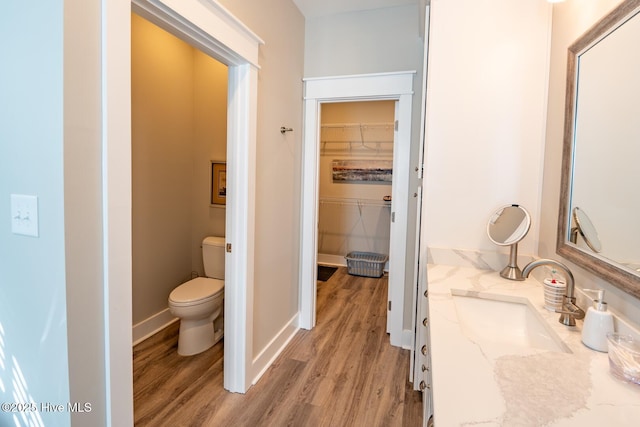 bathroom featuring toilet, wood finished floors, vanity, baseboards, and a spacious closet