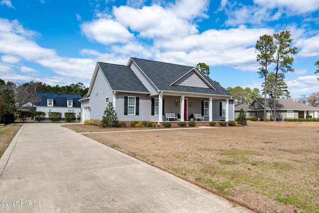 view of front of house with covered porch, driveway, a front lawn, and a shingled roof