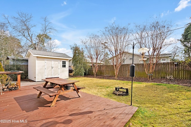 wooden terrace featuring an outdoor fire pit, an outbuilding, a storage shed, a fenced backyard, and a yard