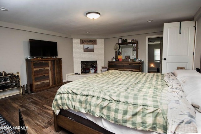 bedroom with dark wood-type flooring and a brick fireplace