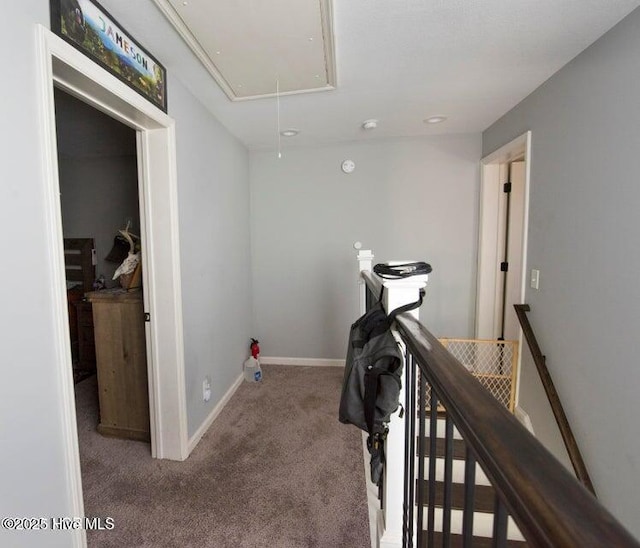 hall with carpet floors, attic access, baseboards, and an upstairs landing