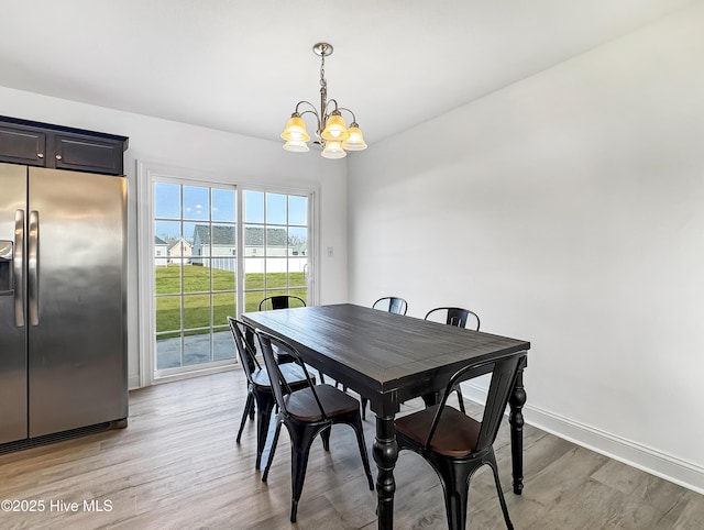 dining space with light wood-type flooring, a notable chandelier, and baseboards