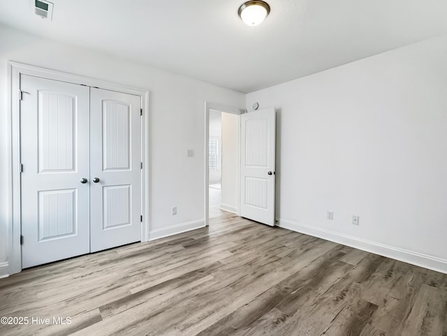 unfurnished bedroom with a closet, visible vents, baseboards, and wood finished floors