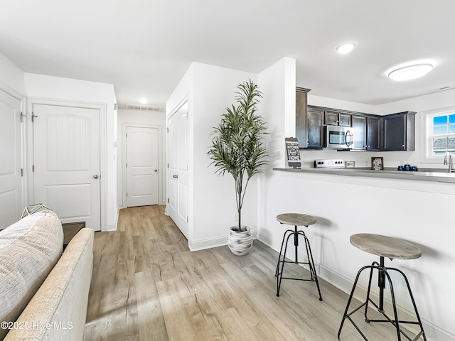 kitchen with a breakfast bar area, light countertops, stainless steel microwave, light wood-style flooring, and baseboards