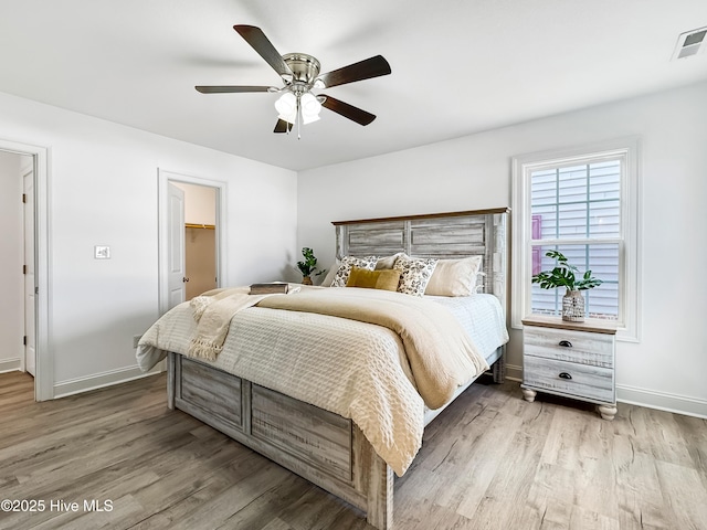 bedroom featuring visible vents, baseboards, a walk in closet, and wood finished floors