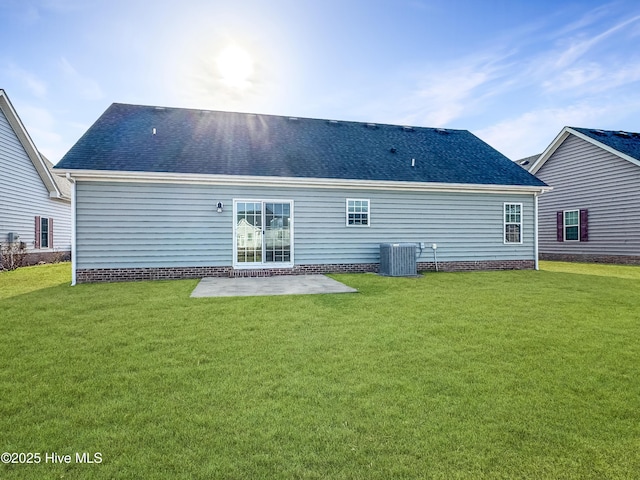 rear view of property with a patio area, roof with shingles, central AC, and a yard