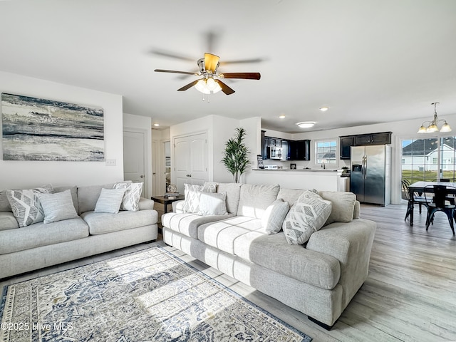 living room featuring recessed lighting, light wood-style flooring, and ceiling fan with notable chandelier