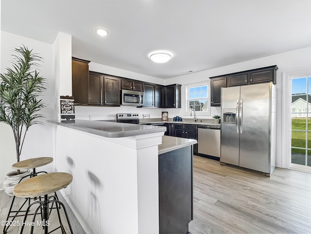 kitchen with dark brown cabinetry, a breakfast bar area, a peninsula, stainless steel appliances, and light wood-style floors