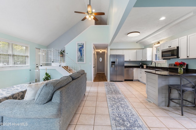 kitchen featuring dark countertops, open floor plan, white cabinetry, stainless steel appliances, and light tile patterned floors