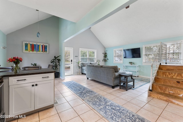 living area with stairway, light tile patterned floors, baseboards, and high vaulted ceiling