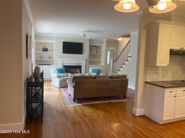 living room with crown molding, baseboards, stairway, a fireplace, and light wood-style floors