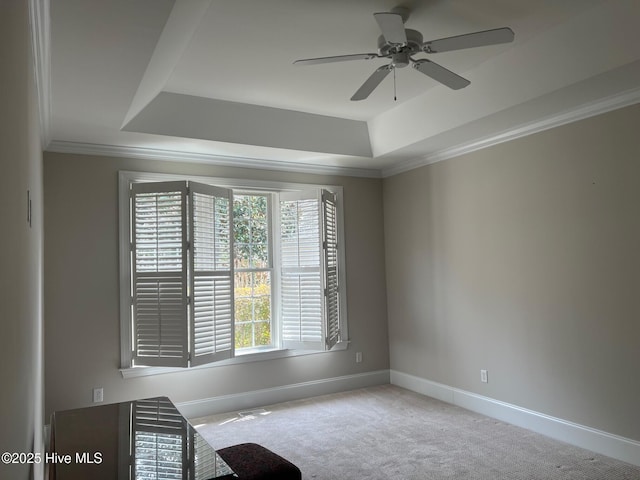 carpeted spare room with a tray ceiling, baseboards, ceiling fan, and crown molding