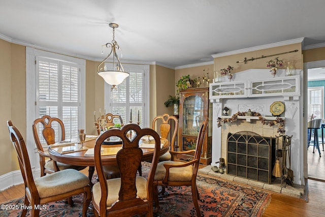 dining area featuring a tile fireplace, crown molding, baseboards, and wood finished floors