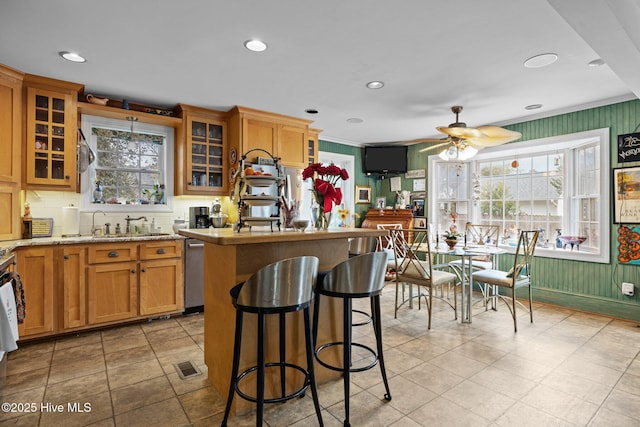 kitchen with a sink, glass insert cabinets, dishwasher, a kitchen breakfast bar, and a center island