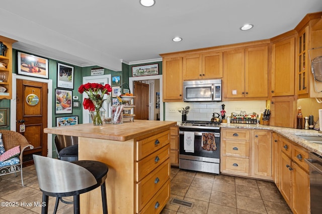 kitchen with a breakfast bar, butcher block counters, decorative backsplash, appliances with stainless steel finishes, and a center island