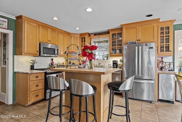 kitchen with backsplash, a center island, appliances with stainless steel finishes, light tile patterned flooring, and light countertops