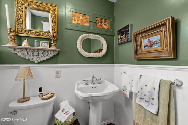 half bath featuring a sink, a wainscoted wall, and toilet