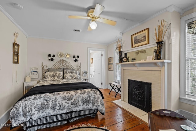 bedroom with baseboards, hardwood / wood-style floors, crown molding, and a tiled fireplace