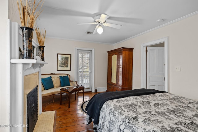 bedroom featuring visible vents, a large fireplace, crown molding, and hardwood / wood-style flooring