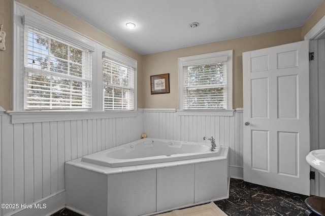 full bathroom with a bath, marble finish floor, and wainscoting