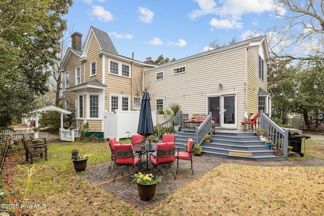 back of house with a deck, a patio, a lawn, and a chimney