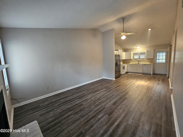 unfurnished living room with baseboards, ceiling fan, dark wood-style flooring, vaulted ceiling, and a sink