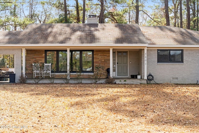 view of front of property with a tile roof, brick siding, a chimney, covered porch, and crawl space