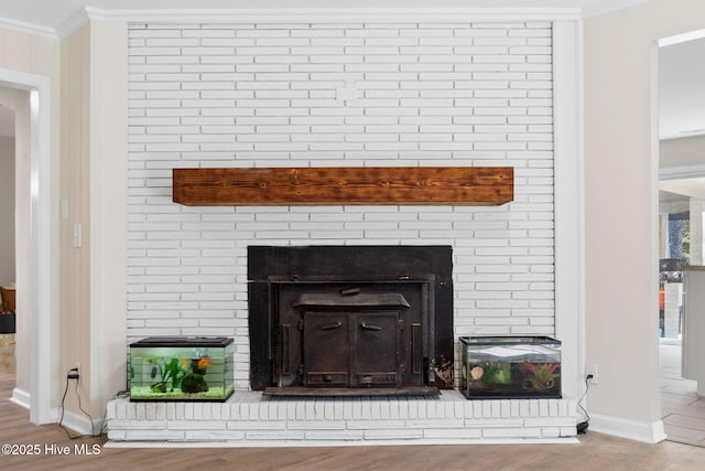 details with ornamental molding, a brick fireplace, wood finished floors, and baseboards