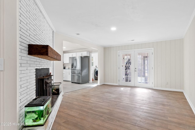 unfurnished living room with washer / dryer, baseboards, ornamental molding, french doors, and light wood-type flooring