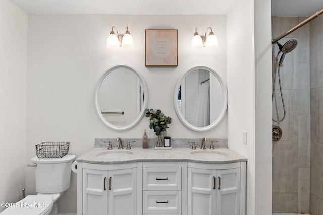 bathroom with tiled shower, a sink, toilet, and double vanity