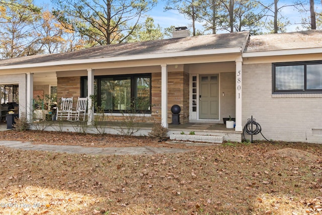 view of exterior entry featuring covered porch, a chimney, and brick siding