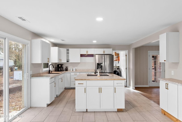 kitchen featuring light countertops, a sink, a kitchen island, washer / dryer, and stainless steel fridge with ice dispenser