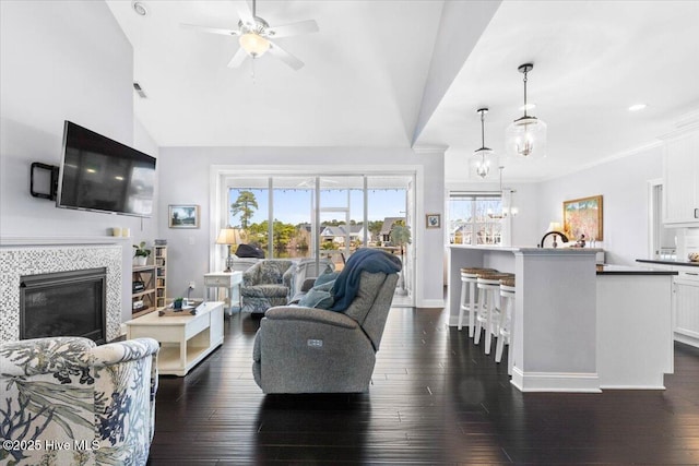 living area with lofted ceiling, ceiling fan with notable chandelier, dark wood-style flooring, visible vents, and a tiled fireplace