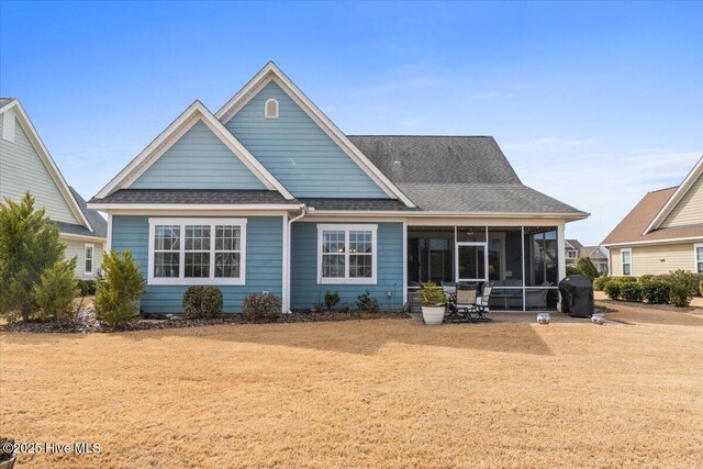 rear view of property with a shingled roof, a lawn, and a sunroom